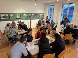 Menschen sitzen in mehreren Kleingruppen an runden Tischen und sprechen miteinander