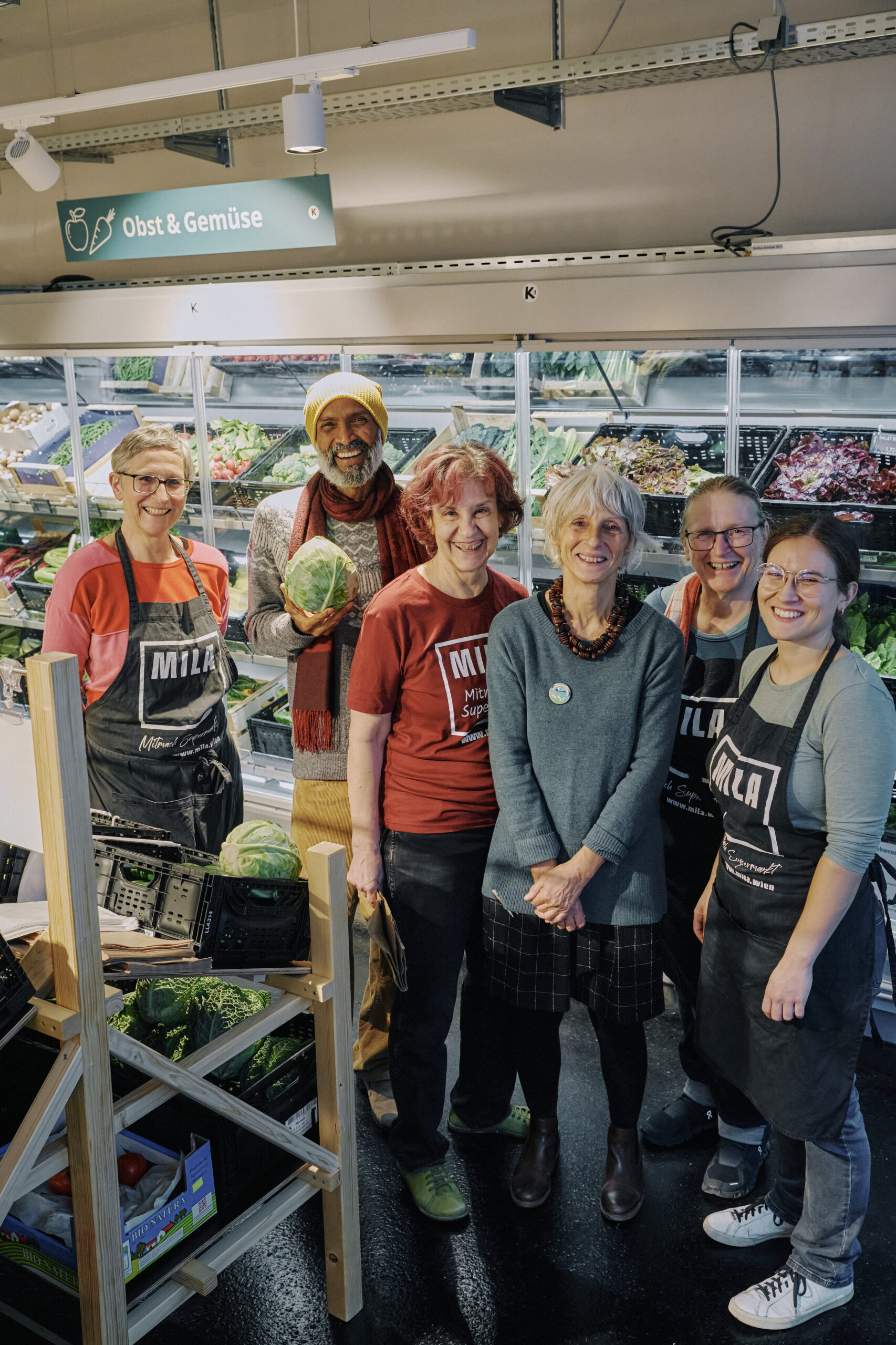 Sechs Menschen stehen in einem Supermarkt vor einem Gemüseregal